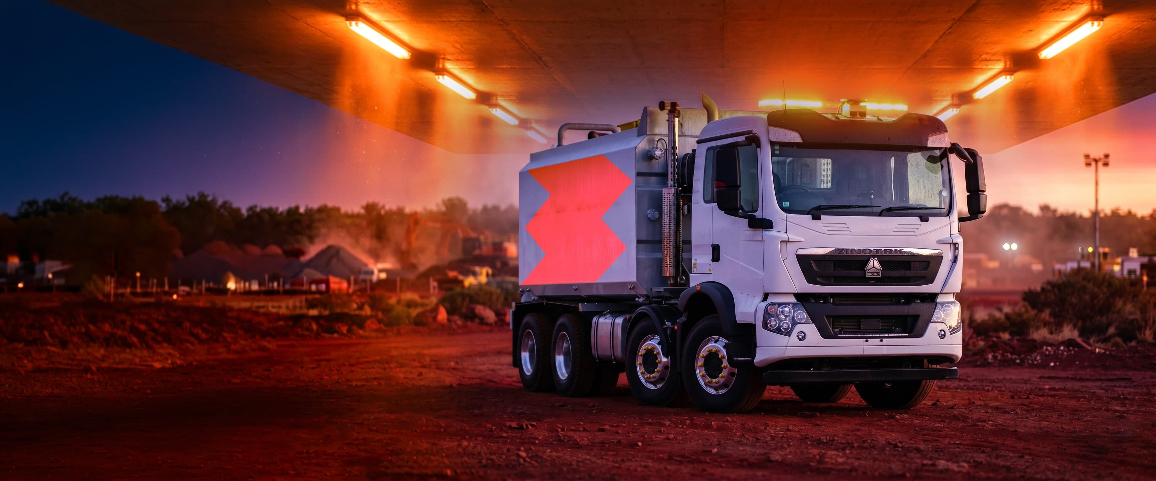 Benang water truck with the orange Benang symbol parked under a highway overpass at dusk