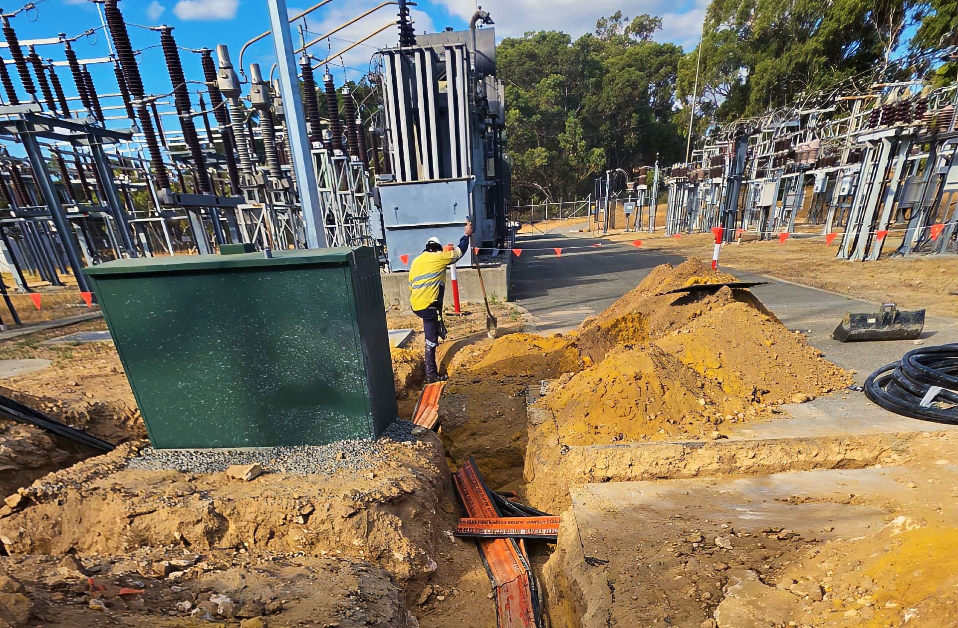 Benang worker backfilling the cable trench beside a green kiosk cabinet inside the Henderson substation