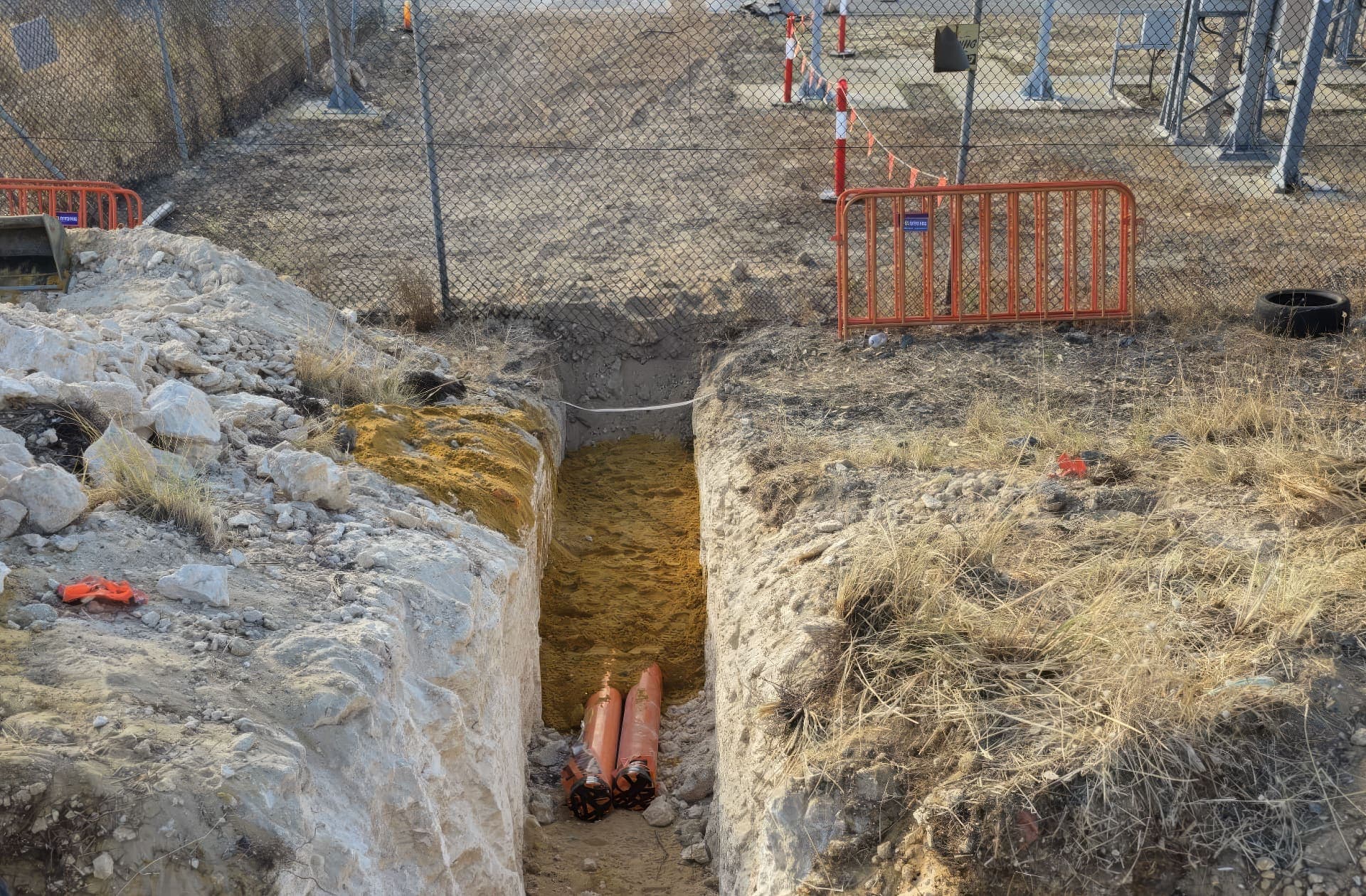 Capped orange conduits at the base of a rock-cut trench outside the substation fence at Henderson