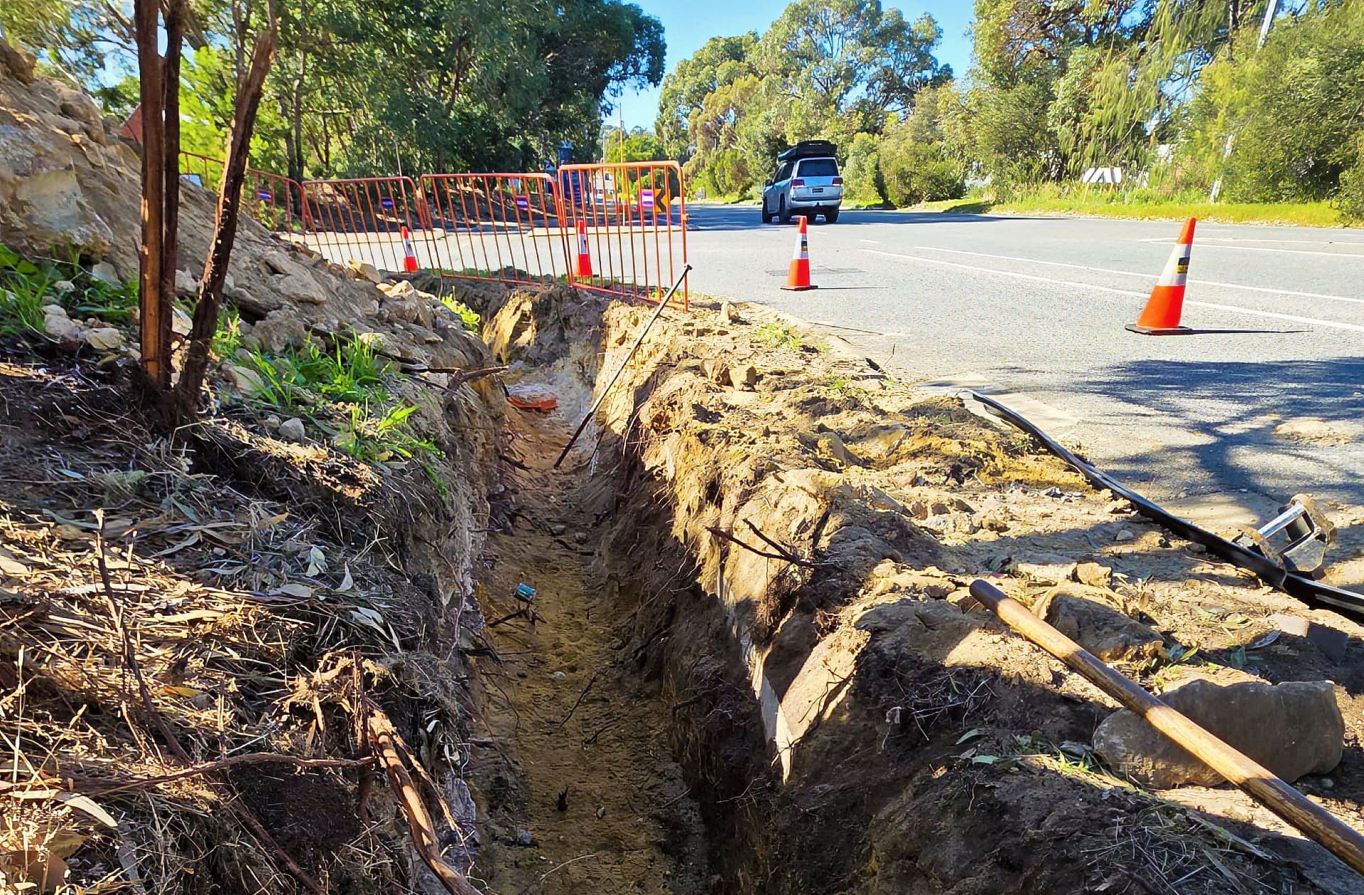 Open cable trench along the verge of Cockburn Road behind barrier fencing and traffic cones