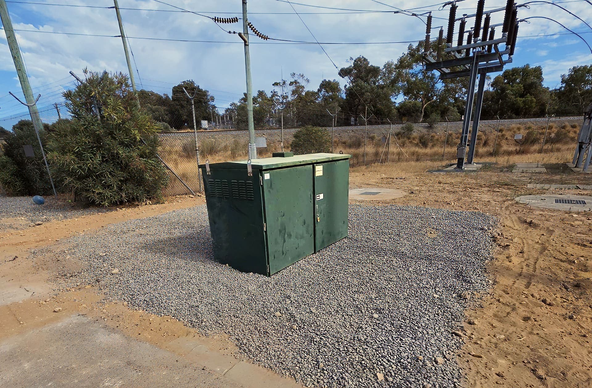 Green kiosk cabinet on a fresh gravel pad beside the rail corridor at Henderson