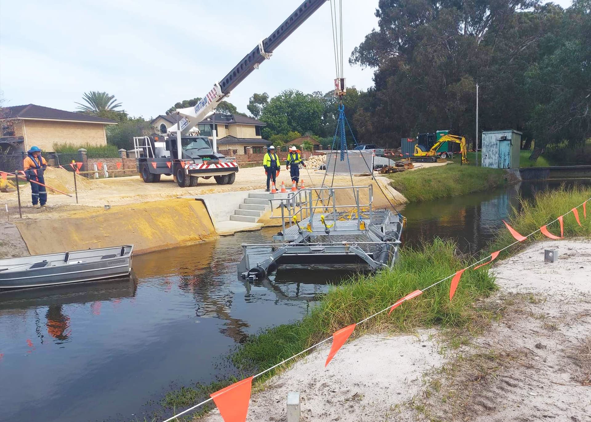 Crane lifting a galvanised litter boom platform into the drain channel at Herdsman Lake