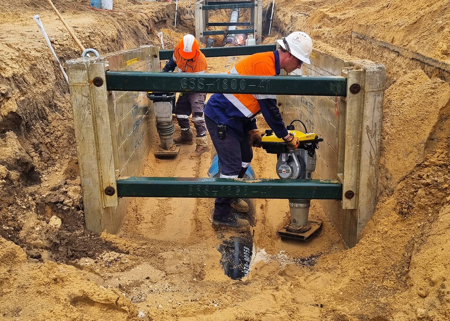 Worker compacting bedding inside a trench shield