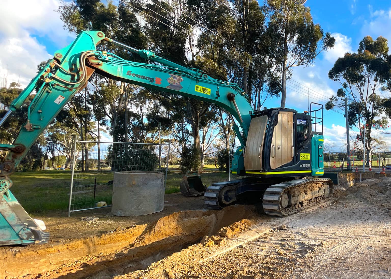 Excavator beside a concrete chamber under street trees