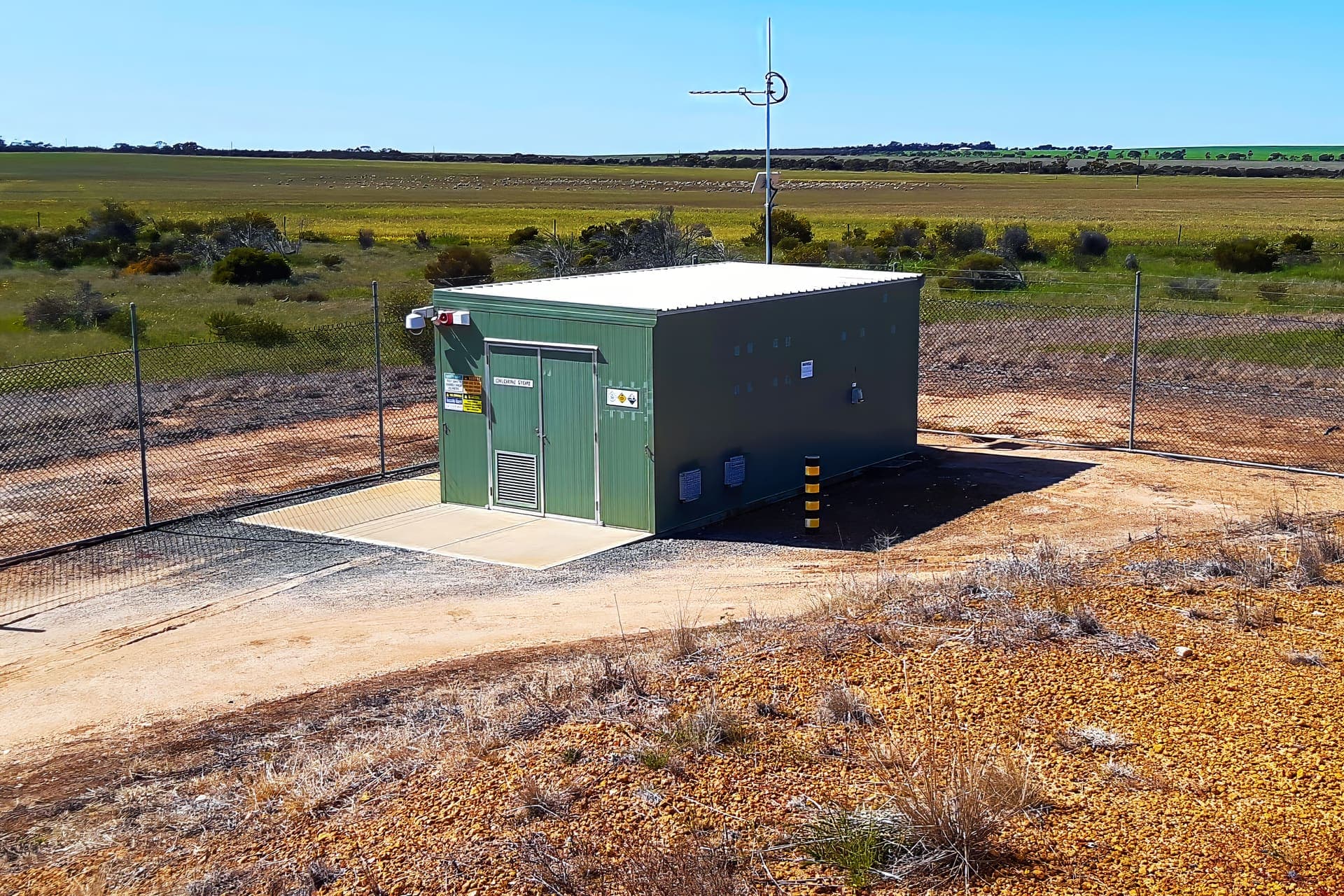 Chlorination facility building inside its security fence with farmland behind