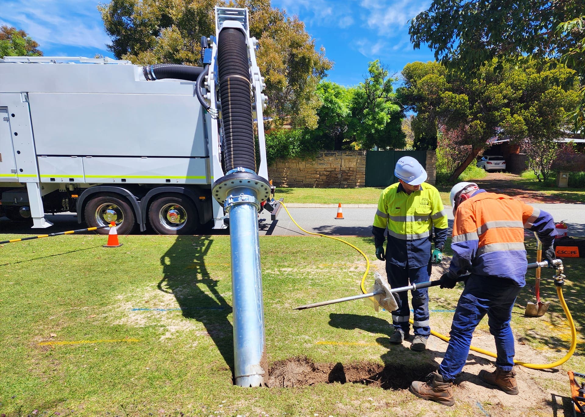 Vac truck boom over a verge excavation with two workers hand exposing a live water main