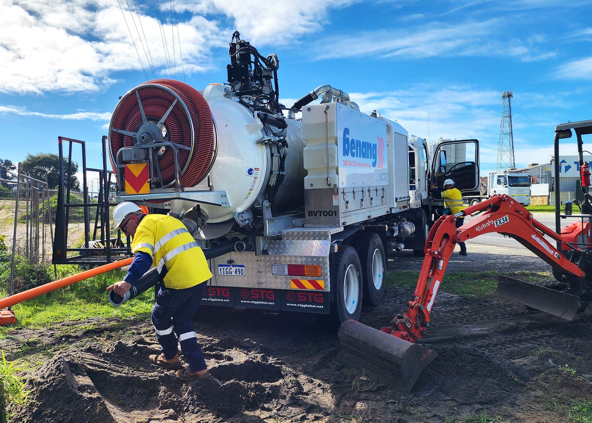Benang worker feeding conduit into the vac truck with the mini excavator alongside