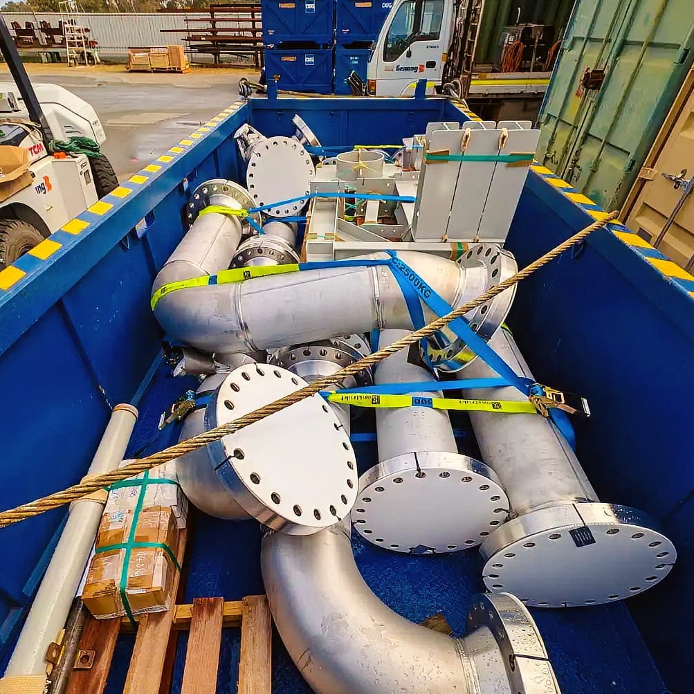 Stainless duplex pipe spools with flanged ends strapped into a blue transport crate at the Benang workshop