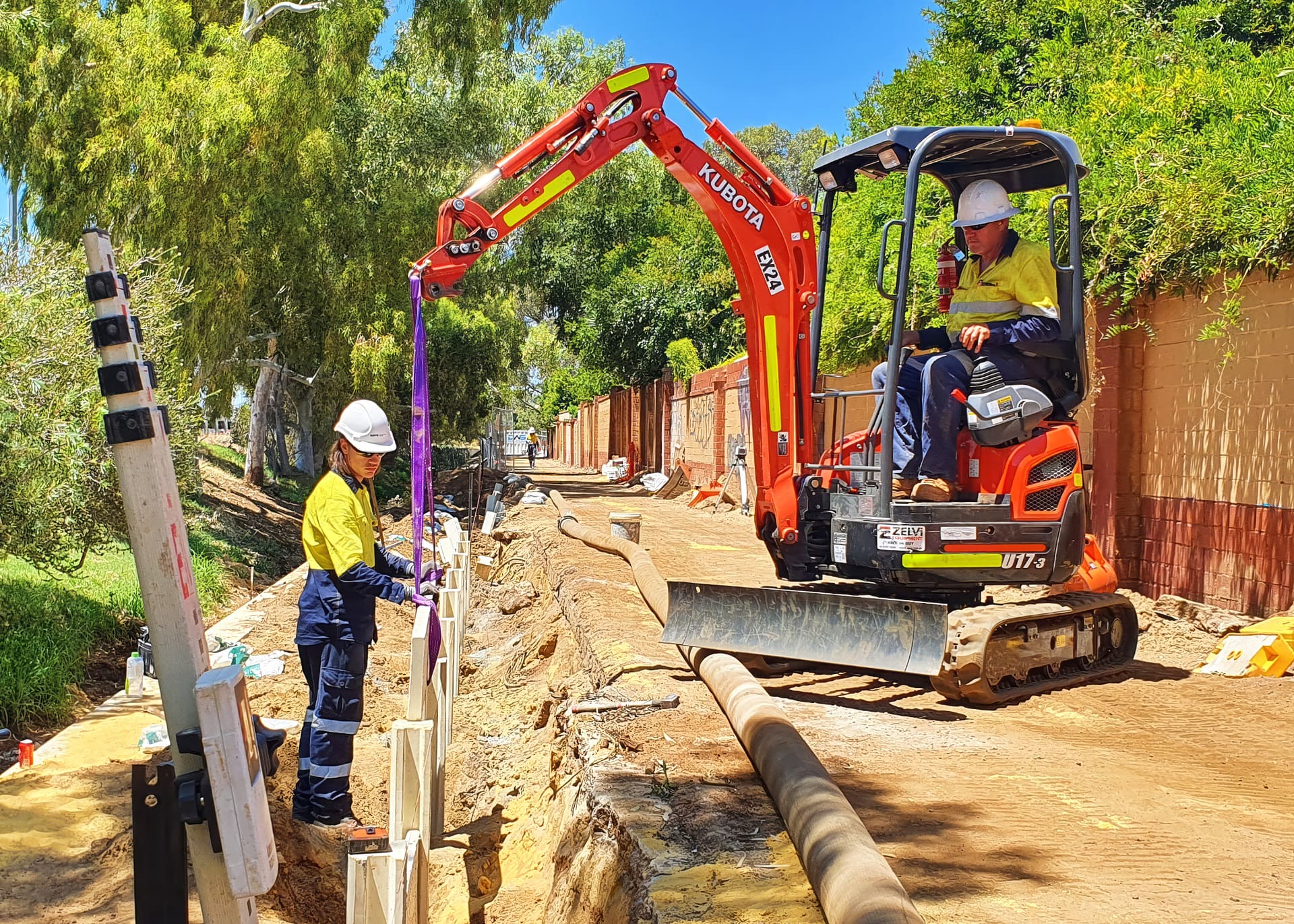 Benang crew slinging a trench shield from a Kubota mini excavator alongside an open pipe trench on the Main Drain upgrade