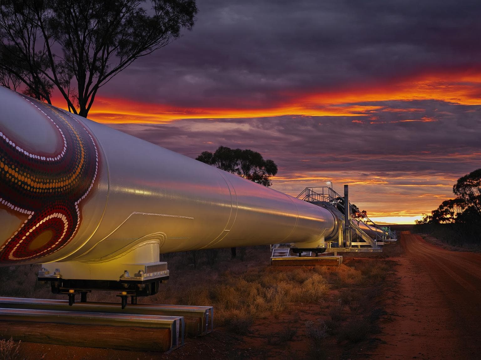 Aboriginal-painted pipeline stretching through the Western Australian outback at sunset
