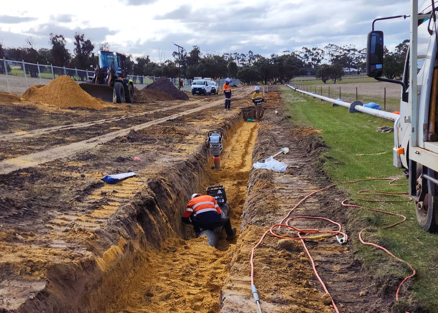 Crew laying pipe along a grassed verge trench at Katanning
