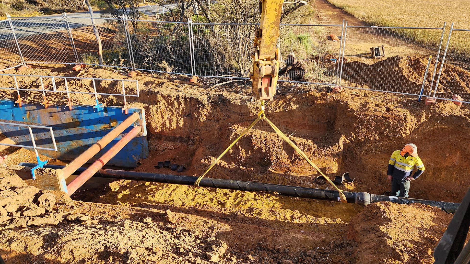 Excavator lowering a new pipe string into the shored trench at Narembeen