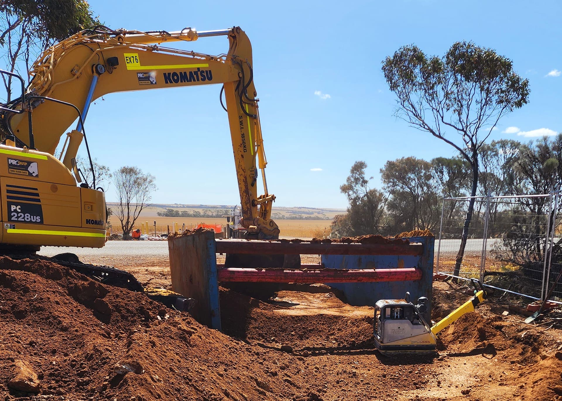 Excavator working over the trench shoring box beside the road at Narembeen